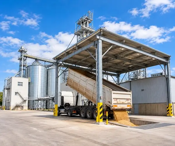 Truck unloading grain into a covered receiving pit beside storage silos